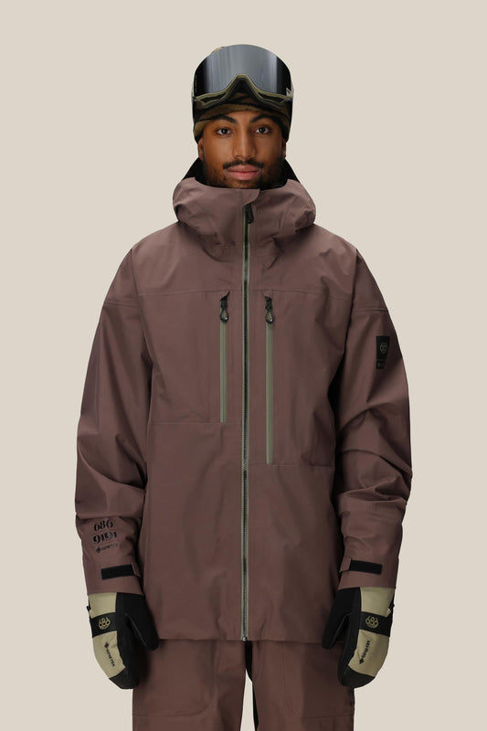 Person wearing a 686 GORE-TEX 3L ATV Thermagraph® Jacket 1 snow jacket, pants, and goggles on a beige background.