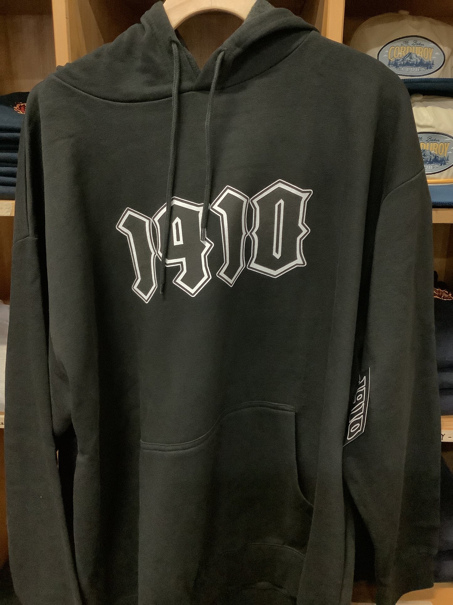 Black hoodie with white 1910 logo on a wooden surface