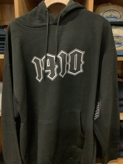 Black hoodie with white 1910 logo on a wooden surface
